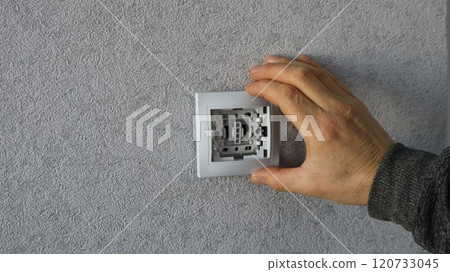 male hand applying white plastic switch housing to base in wall with gray wallpaper, DIY home electrical switch installation male hand applying white plastic switch housing to base in wall with gray wallpaper, DIY home electrical switch installation 120733045