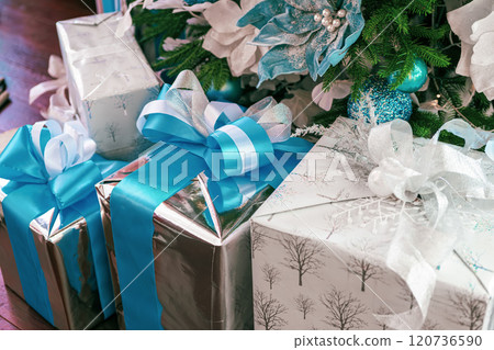 Holiday gifts under a beautifully decorated Christmas tree with silver and blue accents Holiday gifts under a beautifully decorated Christmas tree with silver and blue accents 120736590