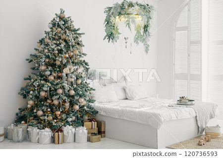 Beautifully decorated Christmas tree and wrapped gifts in bedroom with bed with white linen 120736593