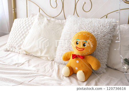 Cozy bedroom with cheerful gingerbread plush toy sitting on bed with decorative pillows 120736616