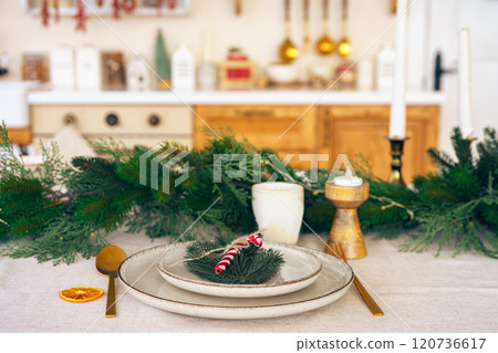 Elegant Christmas holiday table setting with greenery and simple decor on cozy kitchen background Elegant Christmas holiday table setting with greenery and simple decor on cozy kitchen background 120736617