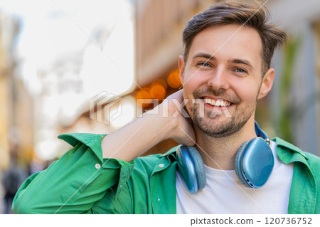 Portrait of smiling young male tourist in casual clothes with wireless headphones around neck 120736752