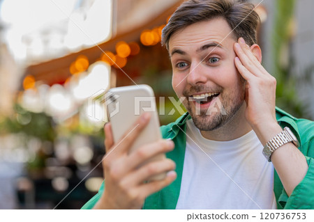 Excited happy winner man using smartphone looking amazed at screen celebrating win good message news Excited happy winner man using smartphone looking amazed at screen celebrating win good message news 120736753