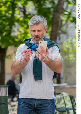 Shocked man trying to pay online shopping with smartphone blocked credit card lack of money balance Shocked man trying to pay online shopping with smartphone blocked credit card lack of money balance 120736754