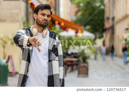 Upset Indian man showing thumb down sign gesture, expressing discontent disapproval in city street Upset Indian man showing thumb down sign gesture, expressing discontent disapproval in city street 120736817