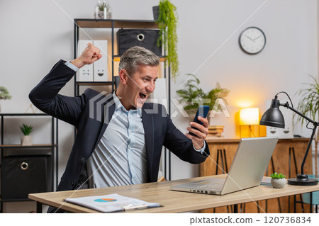 Happy Caucasian businessman celebrating success reading great news on smartphone at home office desk Happy Caucasian businessman celebrating success reading great news on smartphone at home office desk 120736834
