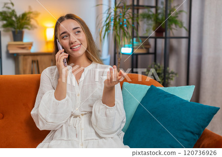 Happy young Caucasian woman making mobile phone conversation with friends sitting on couch at home Happy young Caucasian woman making mobile phone conversation with friends sitting on couch at home 120736926