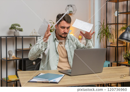 Stressed upset young man freelancer looking at unpaid bank debt bills sitting at home office desk 120736960