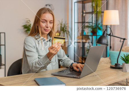 Happy Caucasian woman freelancer using credit card and laptop for online shopping at table at home Happy Caucasian woman freelancer using credit card and laptop for online shopping at table at home 120736976
