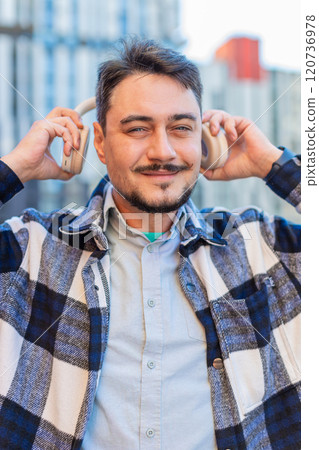 Caucasian mature man taking off wireless headphones looking at camera and smiling on city street Caucasian mature man taking off wireless headphones looking at camera and smiling on city street 120736978