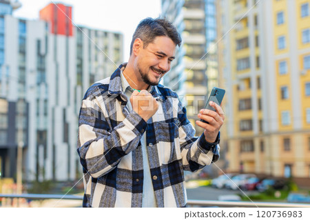 Happy young man using smartphone celebrating victory win good message news on downtown city street 120736983