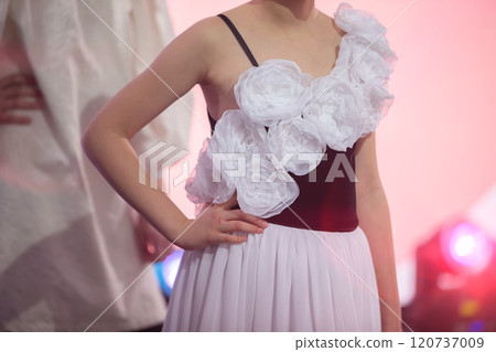 An unrecognizable girl model shows off an evening dress trimmed with white roses made of fabric. An unrecognizable girl model shows off an evening dress trimmed with white roses made of fabric. 120737009