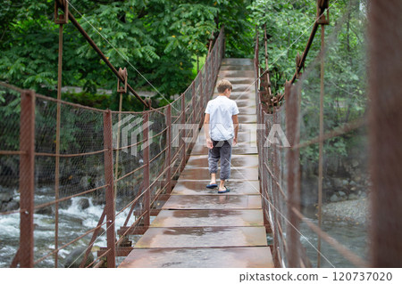 A child walks along a suspension bridge over a mountain river. 120737020