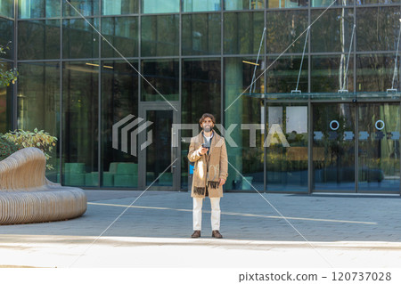 Happy young business man using smartphone and looking at camera while standing in downtown street 120737028