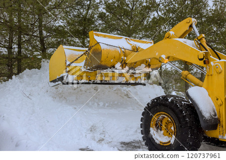 Heavy machinery works to remove thick snow buildup from driveway during winter storm in suburban area. 120737961