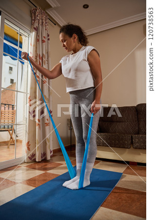 Woman exercising with resistance band in cozy living room 120738563