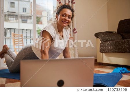 Woman practicing yoga at home with online class on laptop 120738596