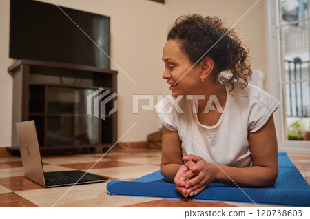 Woman enjoying an online yoga class at home on a laptop Woman enjoying an online yoga class at home on a laptop 120738603