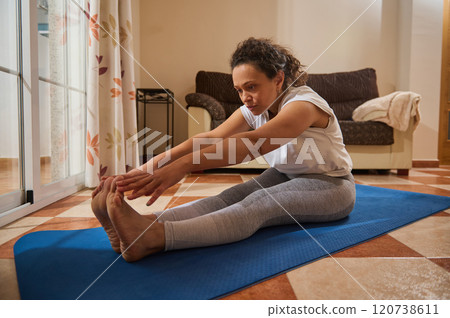 Woman practicing seated forward bend exercise on a yoga mat at home 120738611