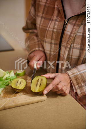 Woman cutting kiwi fruit on a kitchen countertop Woman cutting kiwi fruit on a kitchen countertop 120738634