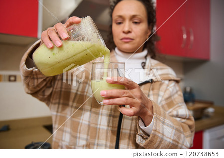 Woman pouring fresh green smoothie in modern kitchen setting 120738653