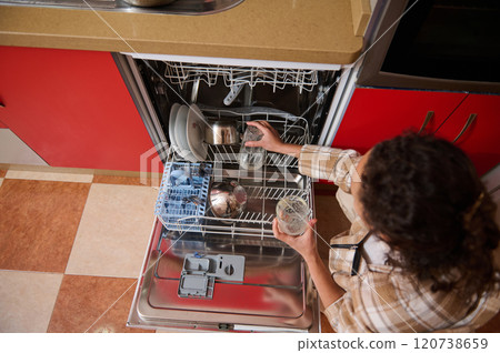 Woman loading dishwasher with glasses in modern kitchen Woman loading dishwasher with glasses in modern kitchen 120738659