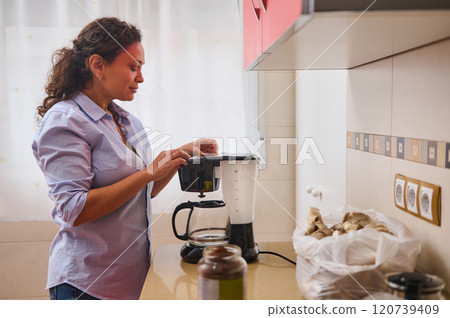 Woman preparing coffee in a cozy home kitchen environment Woman preparing coffee in a cozy home kitchen environment 120739409