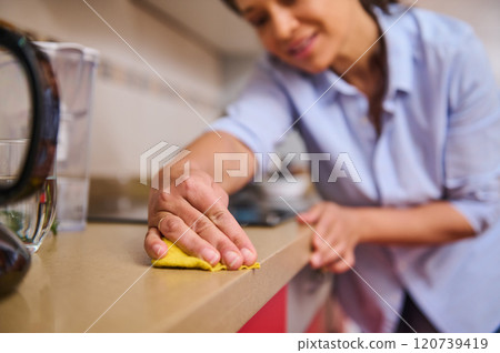 Woman cleaning kitchen counter with yellow cloth at home 120739419