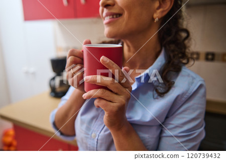 Woman enjoying a cozy moment with hot beverage in kitchen Woman enjoying a cozy moment with hot beverage in kitchen 120739432
