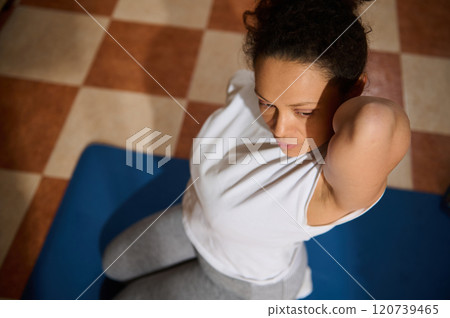 Focused woman doing sit-ups on a blue mat indoors Focused woman doing sit-ups on a blue mat indoors 120739465