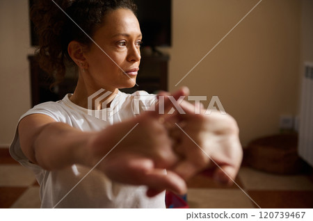 Focused woman stretching arms indoors for relaxation and wellness Focused woman stretching arms indoors for relaxation and wellness 120739467