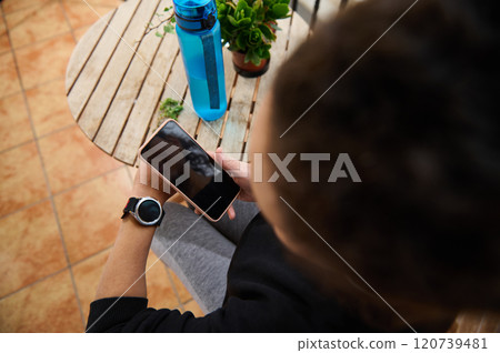 Person checking smartphone while sitting outdoors with smartwatch on wrist 120739481