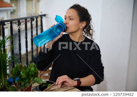 Woman drinking water from a bottle on a balcony 120739482