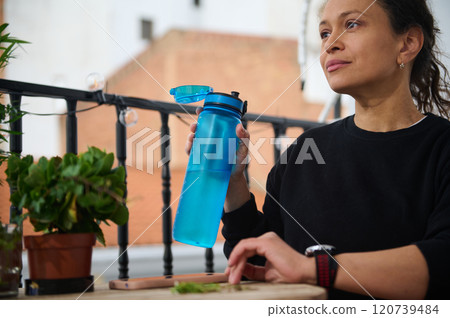 Woman enjoying fresh water on a balcony with greenery and sunlight 120739484