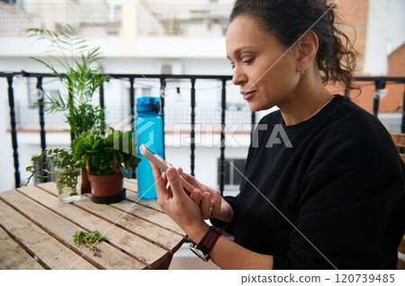 Woman relaxing on balcony using smartphone amidst plants 120739485