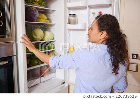 Woman looking inside refrigerator filled with fresh vegetables 120739529