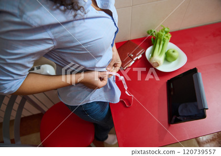 Woman measuring waist with tape near healthy food and tablet 120739557