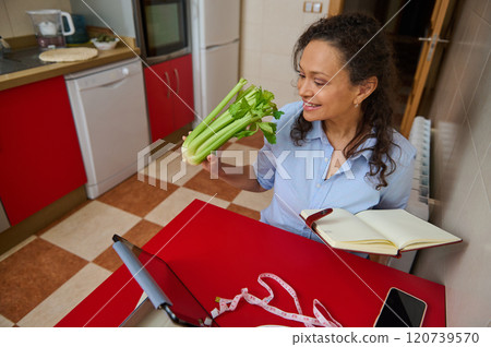 Woman enjoys healthy eating while video chatting in kitchen Woman enjoys healthy eating while video chatting in kitchen 120739570