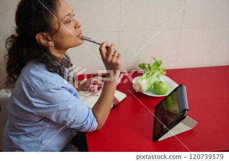 Woman contemplating healthy recipes in kitchen setting with tablet 120739579