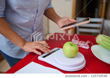 Person using smartphone to weigh green apple on kitchen scale 120739580