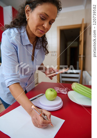 Woman tracking apple calorie intake with smartphone at home Woman tracking apple calorie intake with smartphone at home 120739582