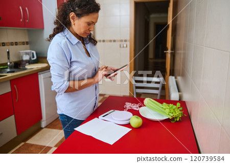 Woman in kitchen with tablet and healthy ingredients on red counter Woman in kitchen with tablet and healthy ingredients on red counter 120739584