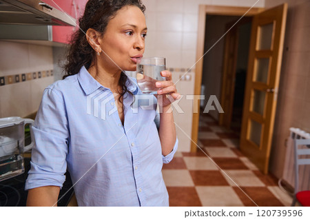 Woman in kitchen drinking a refreshing glass of water Woman in kitchen drinking a refreshing glass of water 120739596
