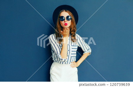 Fashion portrait woman blowing kiss in a black glasses, hat and white skirt on gray background 120739639