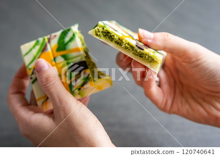 Trend Dubai white chocolate with pistachio paste and kataifi dough in woman hands. Confectionery handmade sweets at home in the kitchen. Trend Dubai white chocolate with pistachio paste and kataifi dough in woman hands. Confectionery handmade sweets at home in the kitchen. 120740641