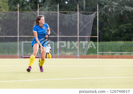 Female athlete in blue uniform running along the pitch during field hockey game 120740657