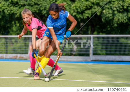 Two young female athletes compete in intense field hockey match during sunny day Two young female athletes compete in intense field hockey match during sunny day 120740661