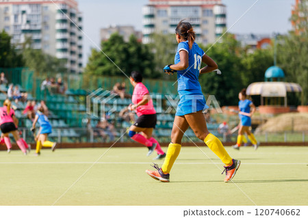 Women playing hockey in colorful uniforms on a sunny day at a local field Women playing hockey in colorful uniforms on a sunny day at a local field 120740662