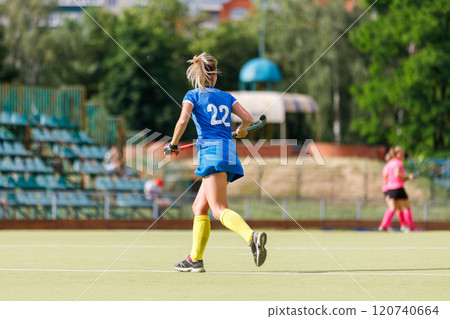 Young female athlete in blue uniform plays field hockey on a sunny day 120740664