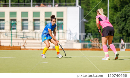 Two young female athletes compete in intense field hockey match during sunny day 120740666